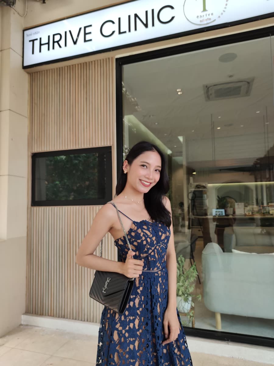 ผู้รับบริการยืนยิ้มหน้าป้าย Thrive Clinic ทางเข้าคลินิก