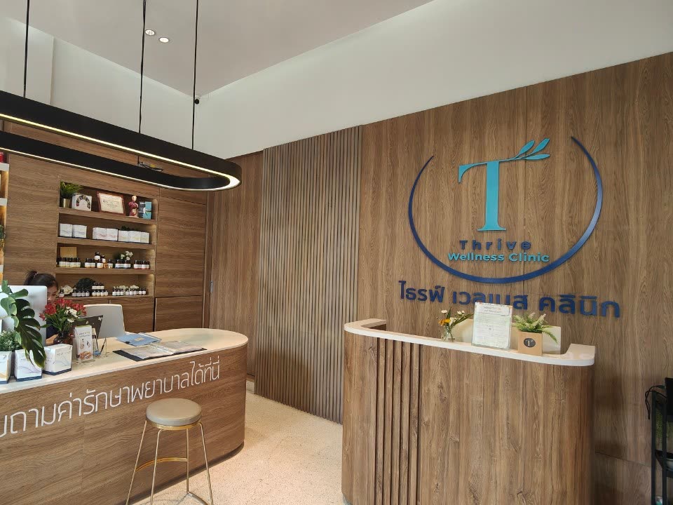 เคาน์เตอร์ต้อนรับไม้โทนอบอุ่นและโลโก้ Thrive Wellness Clinic บนผนัง ที่เดอะ คริสตัล พาร์ค ลาดพร้าว